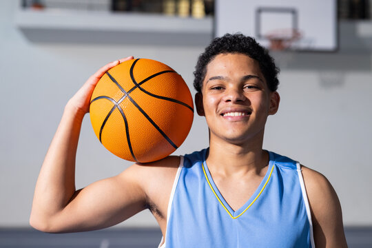 Smiling boy holding basketball in gym, ready for game, enjoying sports