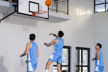 Playing basketball, three young men in blue uniforms shooting hoops indoors