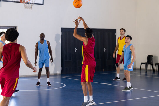 Playing basketball, team in red uniforms shooting ball while others watch