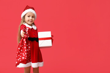 Cute little girl in Santa Claus costume with gift box and bag on red background