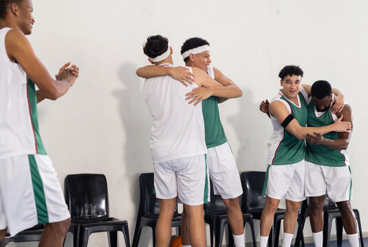 Celebrating victory, basketball team hugging and cheering on court sidelines