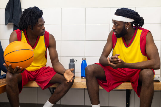 Discussing strategy, african american basketball players in locker room with ball, water bottles - Powered by Adobe