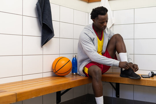 Tying shoelaces, basketball player sitting on bench in locker room with ball, copy space