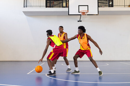 Playing basketball, three athletes in action on indoor court with ball