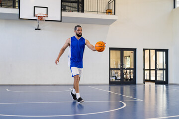 Dribbling basketball, man practicing on indoor court, focusing on skills