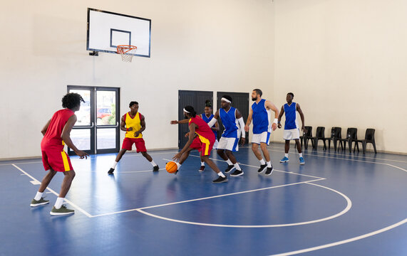 Playing basketball, team in red uniforms dribbling and defending against blue team