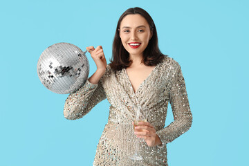 Naklejka premium Beautiful young woman with glass of champagne and disco ball on blue background