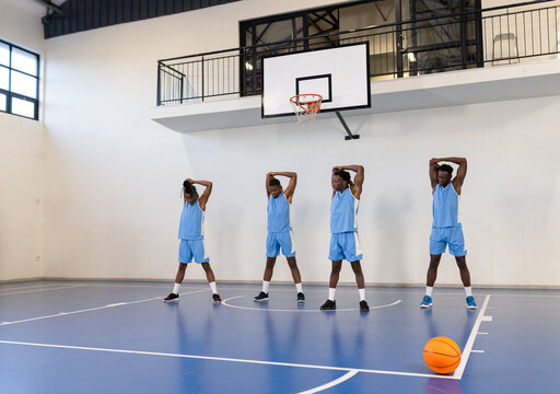 Basketball players stretching on court, preparing for practice session indoors
