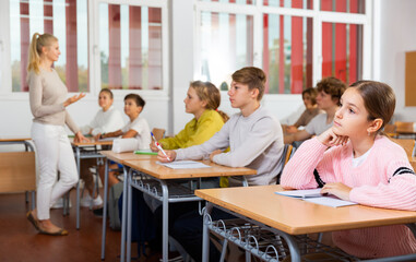 Fototapeta premium Focused teenage students studying in classroom with teacher, writing lectures in workbooks