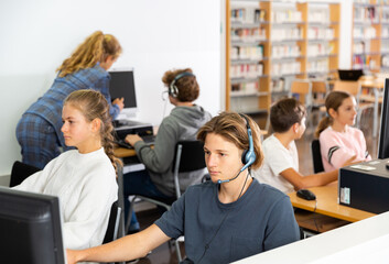 Obraz premium Portrait of a fifteen-year-old schoolboy in headphones, studying at a computer in the classroom at a informatics lesson