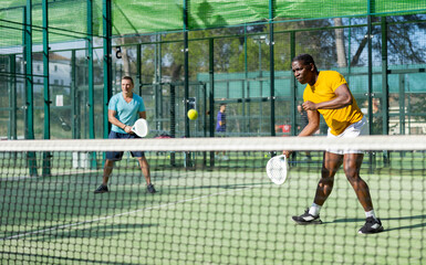 Obraz premium African-american man in sportswear playing padel tennis match with partner during training on court.