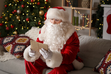 Santa Claus with letters sitting on sofa at home