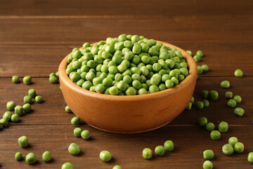 Fresh green peas in bowl on wooden table
