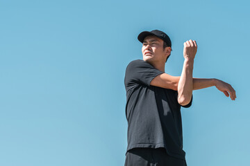 青空の下でストレッチするスポーツウェア姿の中年男性
