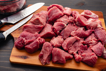 Many Chunks of Pork Shoulder with Knives on a Cutting Board: Pieces of Boston butt with a boning knife and a santoku knife on a wood chopping board