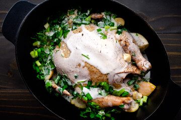 Uncooked Chicken in a Dutch Oven with Herbs and Coconut Milk: Raw chicken in a cast iron pot with coconut milk, cilantro, scallions and lemon wedges