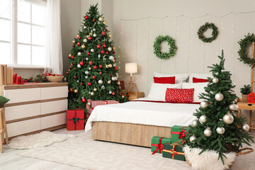 Interior of stylish bedroom with Christmas trees, glowing garland and mistletoe wreaths
