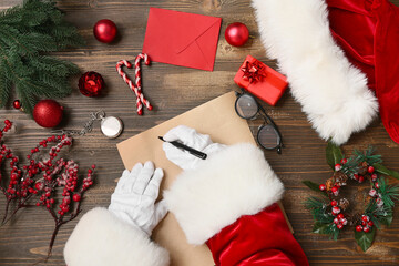 Santa Claus with Christmas decorations and pocket watch writing letter on brown wooden background