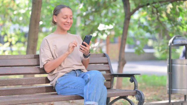 Young Hispanic Woman Celebrating Success on Phone while Sitting Outdoor