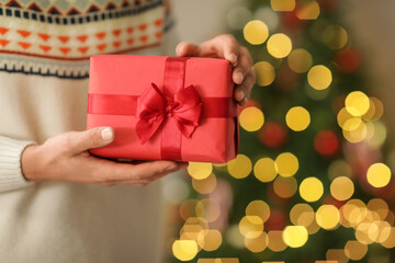 Man giving gift box near Christmas tree at home, closeup