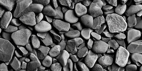A close-up view of various smooth river stones in shades of gray, creating a textured surface in natural light