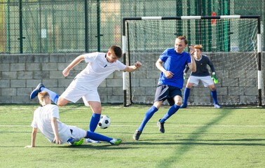 Game moments of football match between two teams of teenagers in white and blue shirts