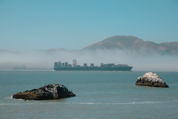 A Tranquil Harbor Scene

This serene image captures a peaceful moment on the water. A large cargo ship sails majestically through the calm bay, its journey shrouded in a light mist.