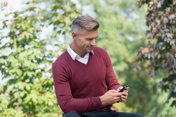 Autumn man use phone. Businessman in casual style. Businessman texting on phone outdoor. Business communication style. Online business. Business man use phone in autumn. Smiling manager