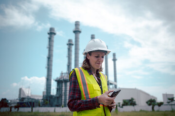 Engineers wearing safety gear, including hard hats examining survey a large blueprint tablet standing industrial facility gas or oil refinery engaged in a job requires high safety standards concept