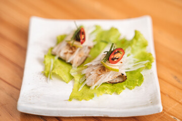 Gourmet appetizer on a white plate with lettuce, thinly sliced meat, and chili garnish.