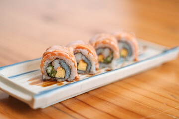 Four sushi rolls with salmon on a rectangular plate, drizzled with sauce.