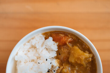 White rice with black sesame seeds and vegetable curry in a bowl on a wooden surface.