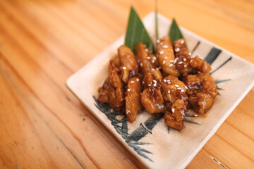 Glazed chicken pieces with sesame seeds on a blue and white patterned plate, garnished with green leaves.