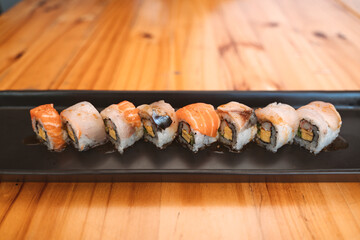 Sushi rolls with salmon, white fish, and avocado on a black rectangular plate.