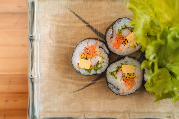 Maki sushi rolls with vegetables and seafood on a beige cloth with green leafy garnish.
