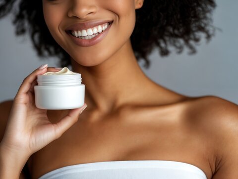Linda mulher negra com sorriso no rosto segurando um creme corporal, em um fundo cinza. A imagem celebra a beleza natural da pele negra e o ato de cuidar de si, promovendo autoaceita&ccedil;&atilde;o e bem-estar.