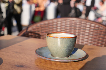 A closeup of a beautifully crafted coffee cup on a table in a vibrant, busy outdoor setting