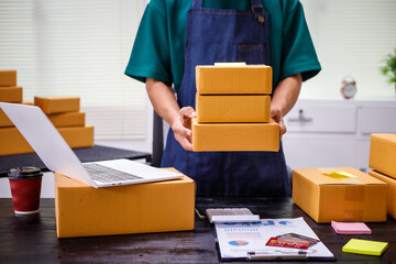close-up of a man's hands working meticulously with a cardboard box on wooden desk, representing an...