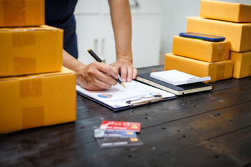 close-up of a man's hands working meticulously with a cardboard box on wooden desk, representing an...