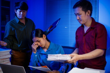 businessman and an Asian businesswoman work late into the night at the office, stressed and busy,...