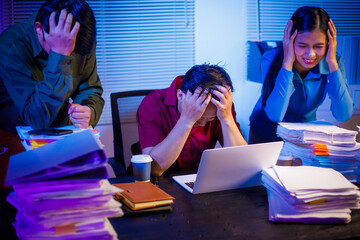 businessman and an Asian businesswoman work late into the night at the office, stressed and busy,...