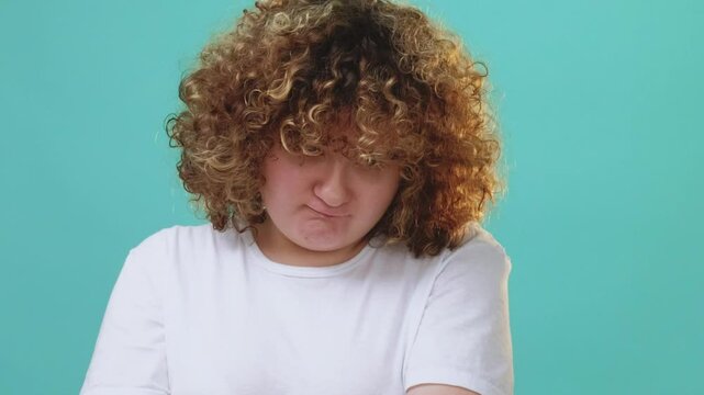 Offended expression. Grumpy face. Body shaming. Frowning upset overweight shy chubby girl with crossed arms isolated on blue free space background.