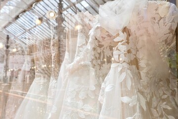 Close-up of lace, sheer fabric and silk chiffon wedding dresses on display at an upscale luxury...