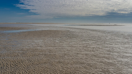The time of low tide in the ocean. A pattern of twisted sand ridges formed on the exposed seabed. Puddles of water on wet sand.  Blue sky, clouds. Madagascar. Morondava. The Mozambique Channel.