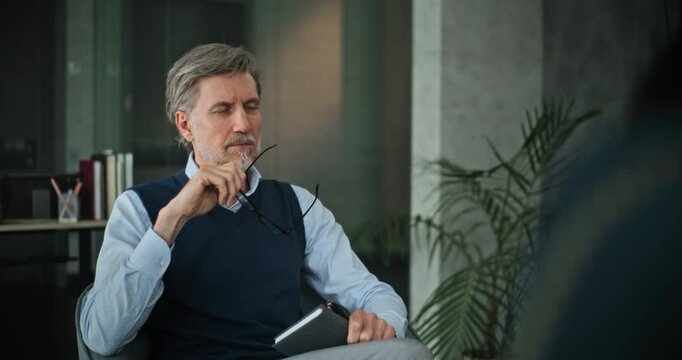 Professional marriage counselor sits in chair, listens attentively to patients on counseling session. Mature psychologist analyzes problem, provides group therapy for couple. Psychology concept.