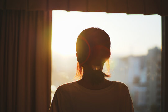 窓から夕日を見る女性のシルエット