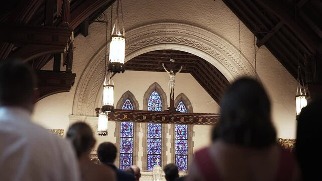 A group of people stand in church pews during a catholic ceremony or mass looking at Jesus on the cross.