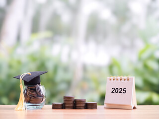 2025 Desk calendar, Glass bottle with graduation hat and stack of coins. The concept of saving money for education, student loan, scholarship, tuition fees in the future
