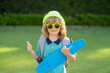 Childhood and fashion. Cute child with skateboard on summer park background. Funny kid boy, stylish skater holding skateboard outdoor. © Volodymyr
