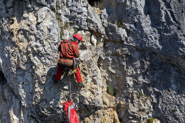 Aerial view of mountain rescuer abseiling on a rocky wall hanging on a rope